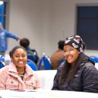 Three college students sitting together in a large conference room, smiling